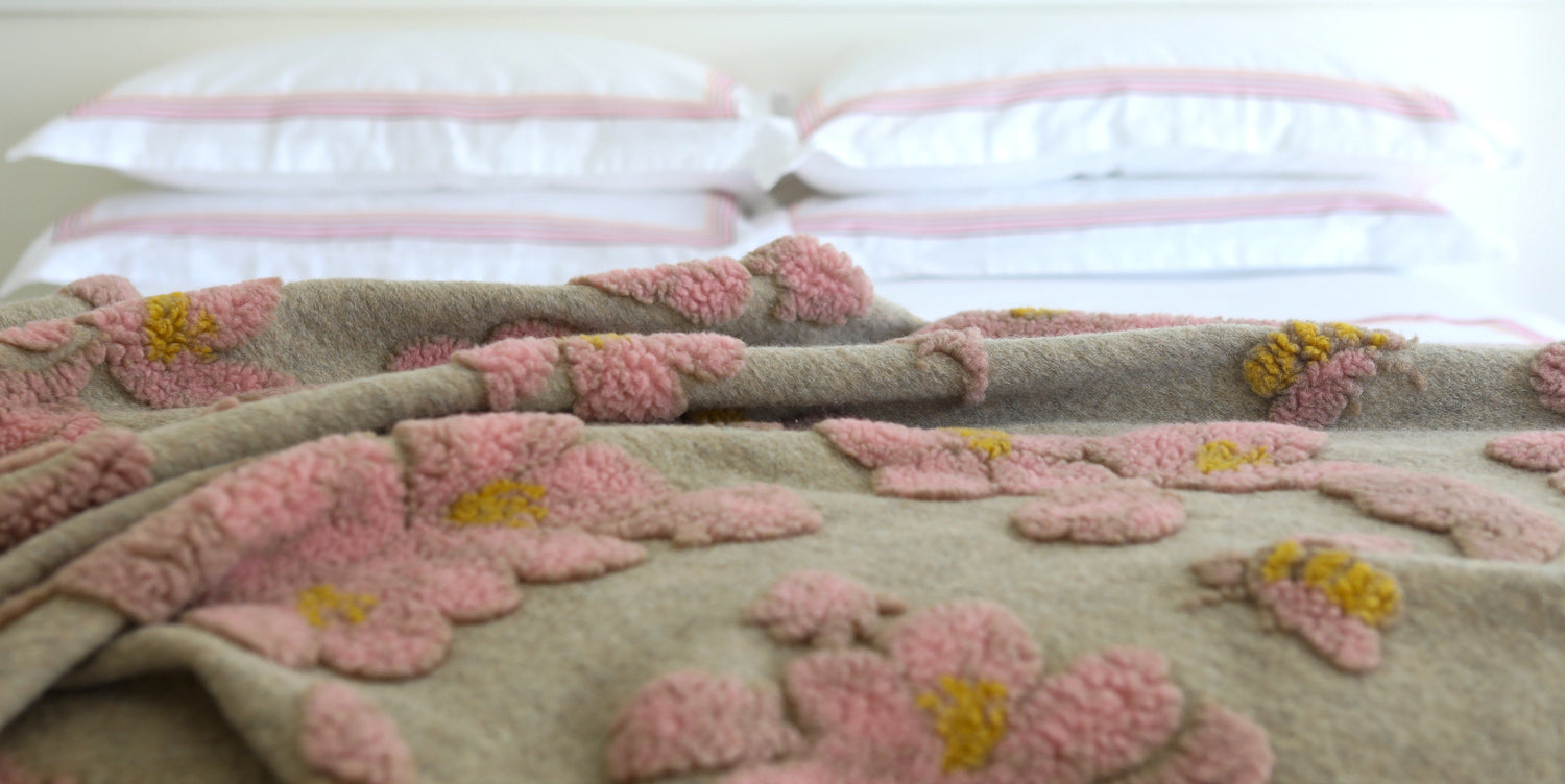Sand coloured boiled wool  throw with detailing of pink flowers and yellow bees finished with a pink blanket sticking along the edge.