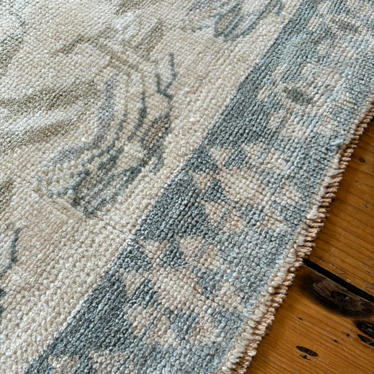 Close-up of a textured rug with a geometric pattern on a wooden floor.