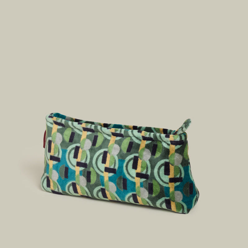 A small zippered pouch with a colorful geometric pattern in teal, green, yellow, black, and gray, set against a solid light beige background.