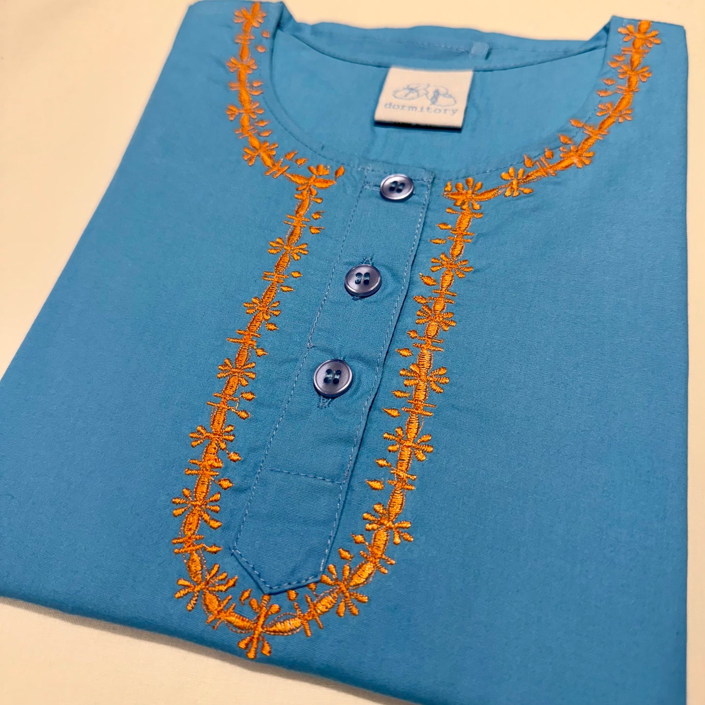 Children's pyjamas in turquoise cotton fabric with orange embroidery around the neck