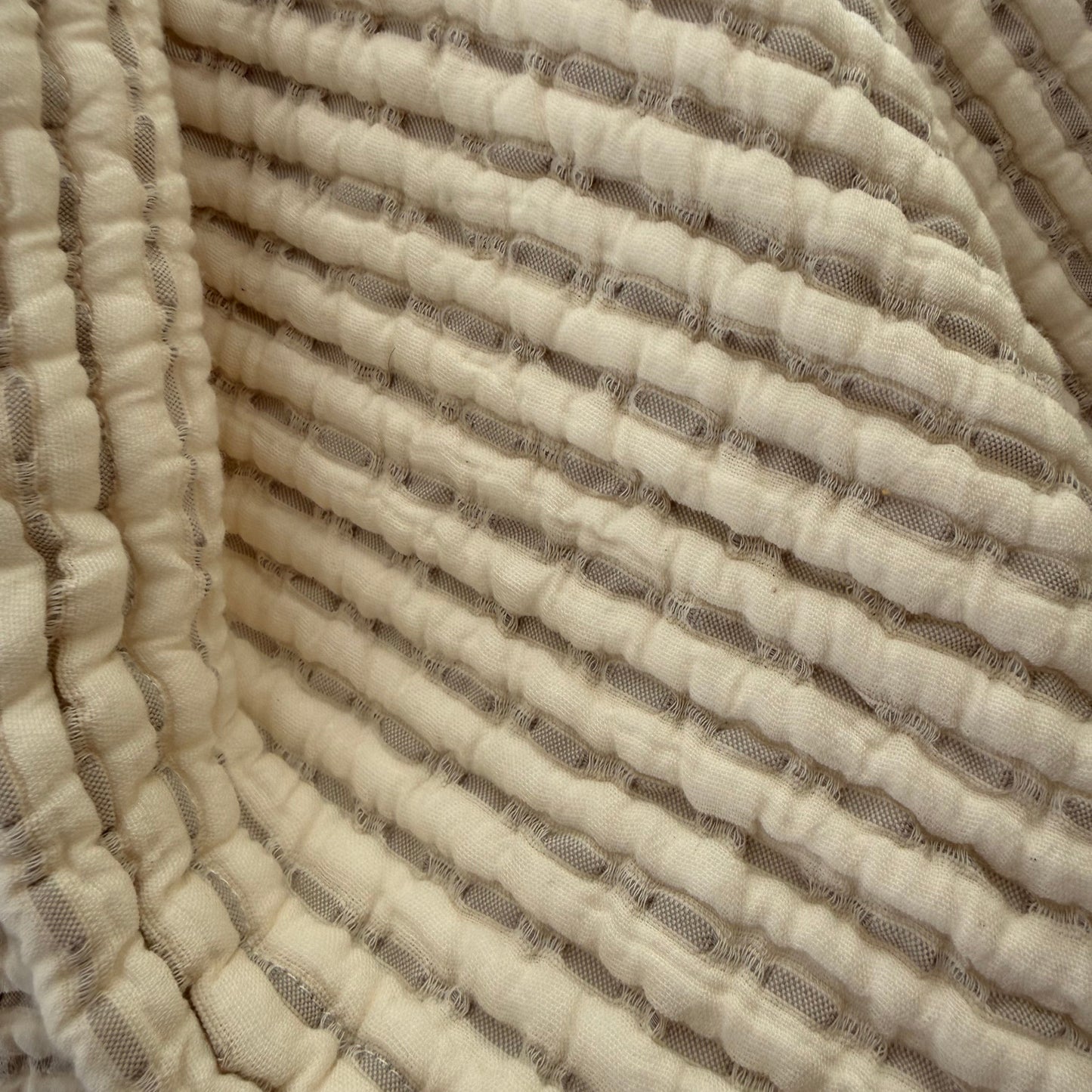 Close up of cream cotton bedspread with a woven beige stripe showing the coloured stripe detailing.
