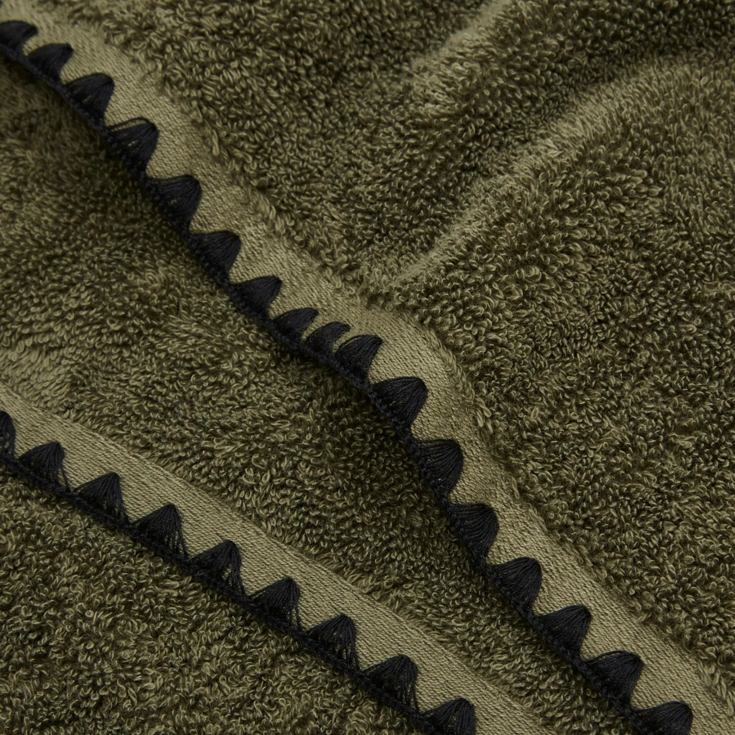 Khaki green towel zoomed in highlighting the embroidered edge detailing on the towel.