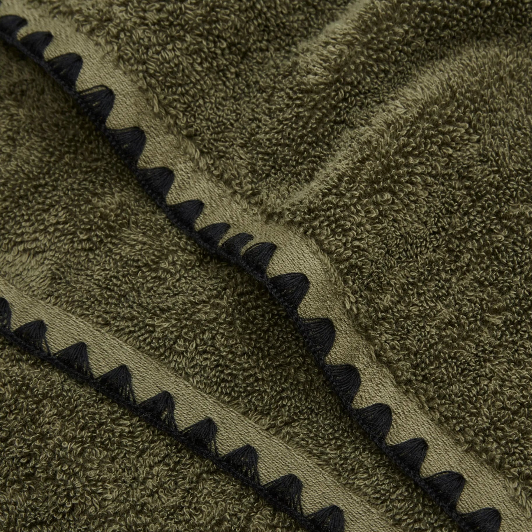 Khaki green towel zoomed in highlighting the embroidered edge detailing on the towel.