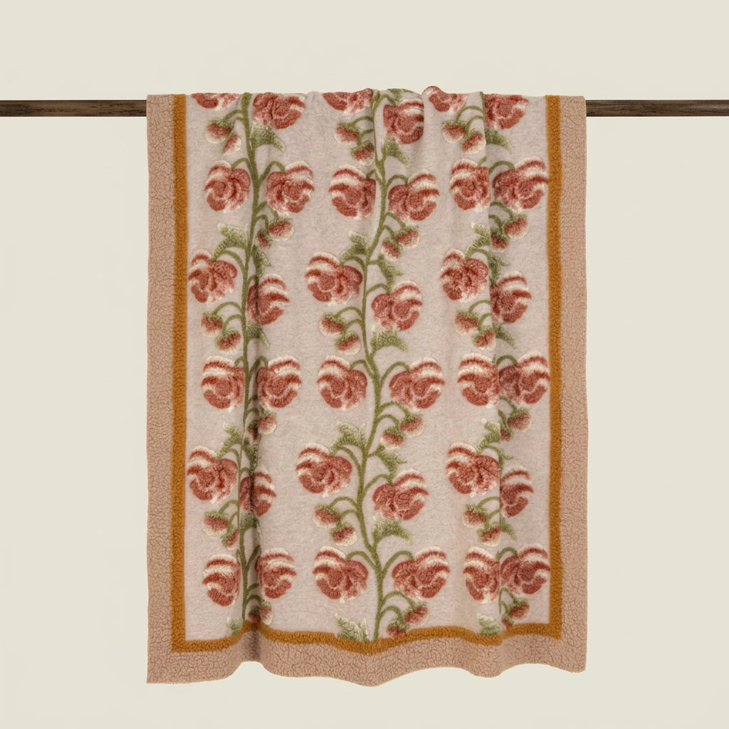 A woven textile panel, a wool trhow, featuring a vertical floral pattern with terracotta flowers, green stems, and a mustard-gold border on a light beige background, hanging from a dark wooden rod.