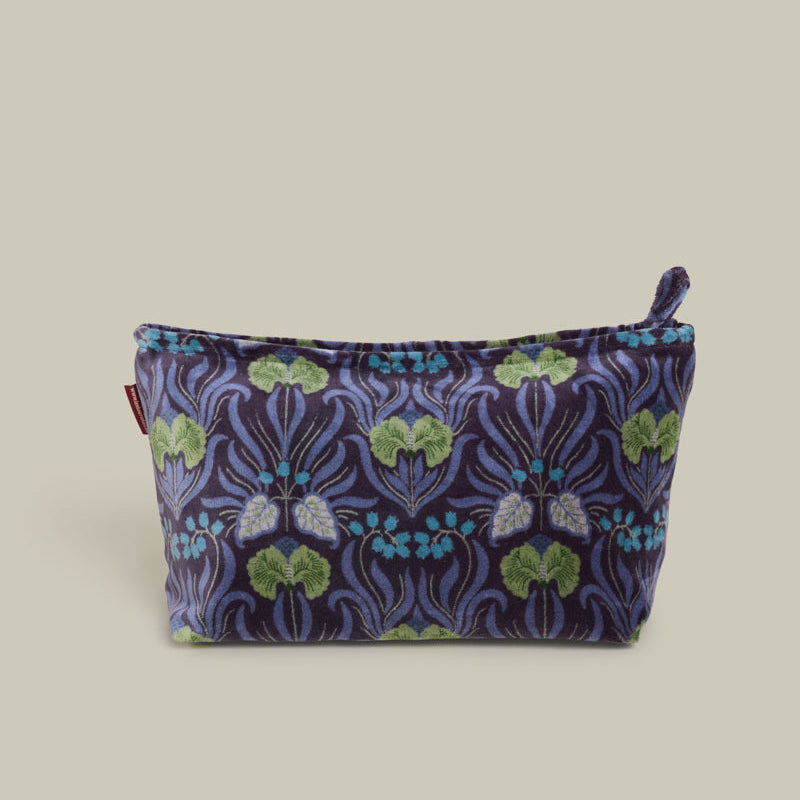 A small zippered cosmetic pouch with a dark purple and blue floral pattern, green leaves, and butterfly motifs, shown on a solid beige background.