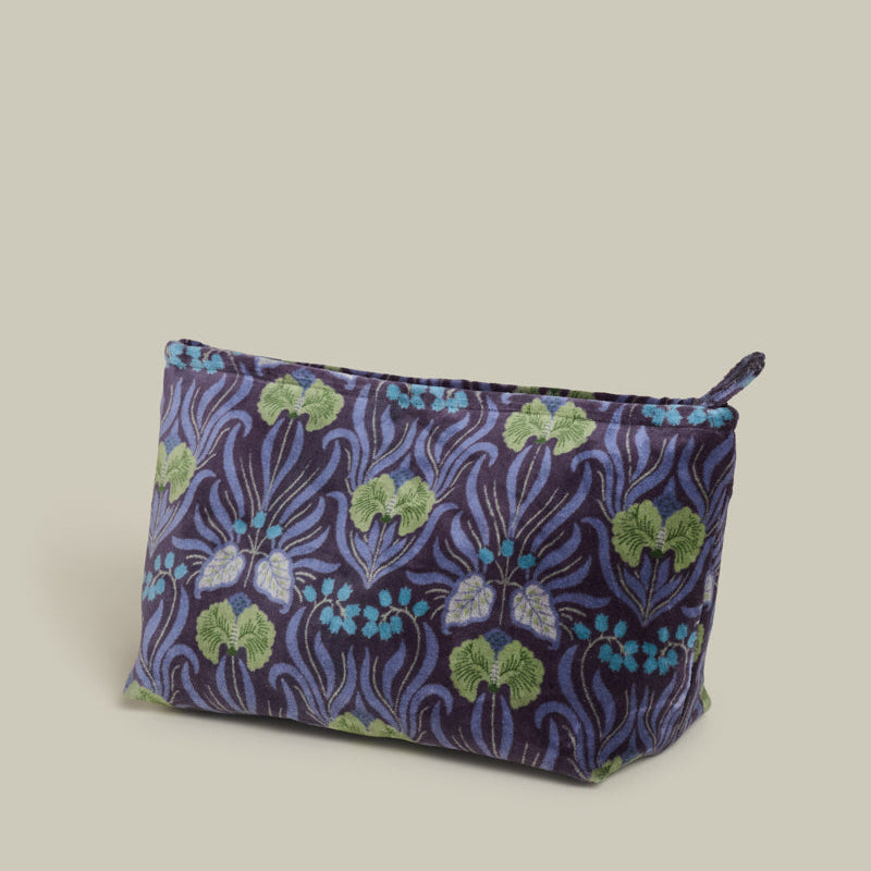 A small zippered cosmetic pouch with a dark purple and blue floral pattern, featuring green and light blue accents, set against a solid beige background.