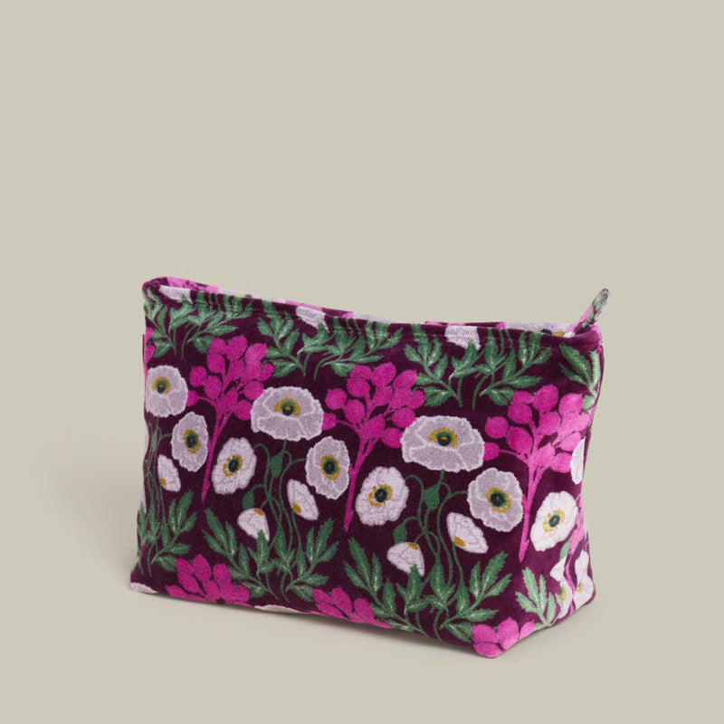 A small zippered pouch with a dark purple velvet-like fabric covered in a pink, white, and green floral print, shown on a solid light beige background.