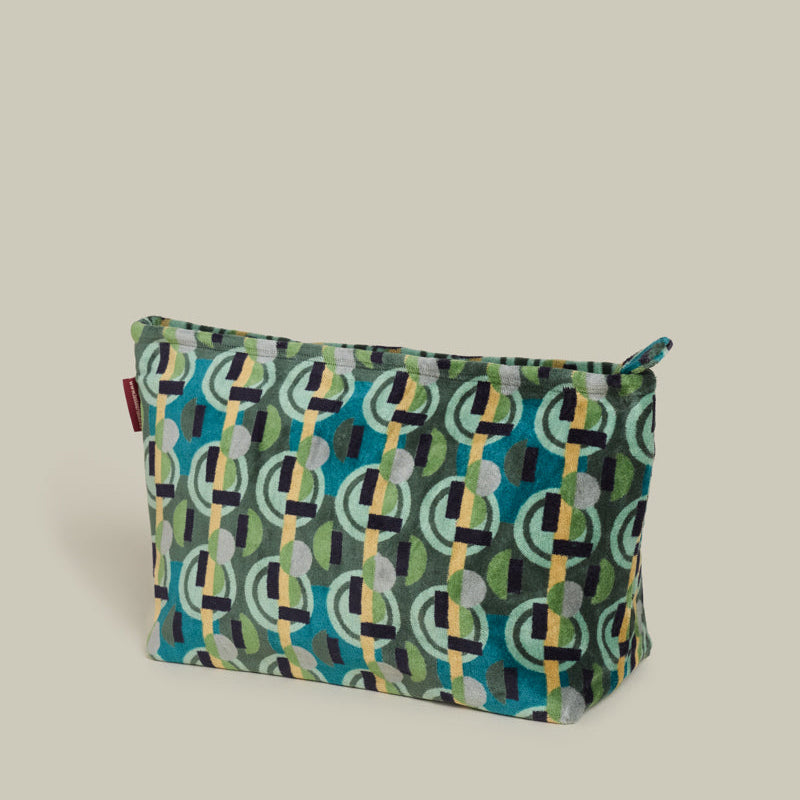 A zippered pouch with a colorful geometric pattern featuring teal, green, black, and yellow shapes, set against a solid light beige background.