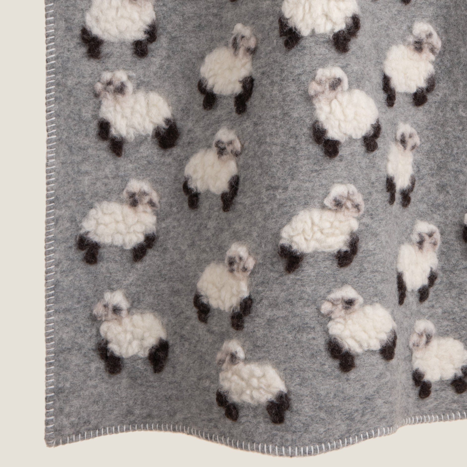 Grey wool blanket with lamb motifs patterned throughout, finished with a white blanket stitched edge.