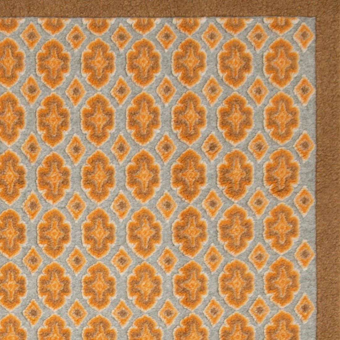 A close-up of a patterned rug or textile with repeating orange and tan medallion motifs on a light gray background, bordered by a solid brown edge.