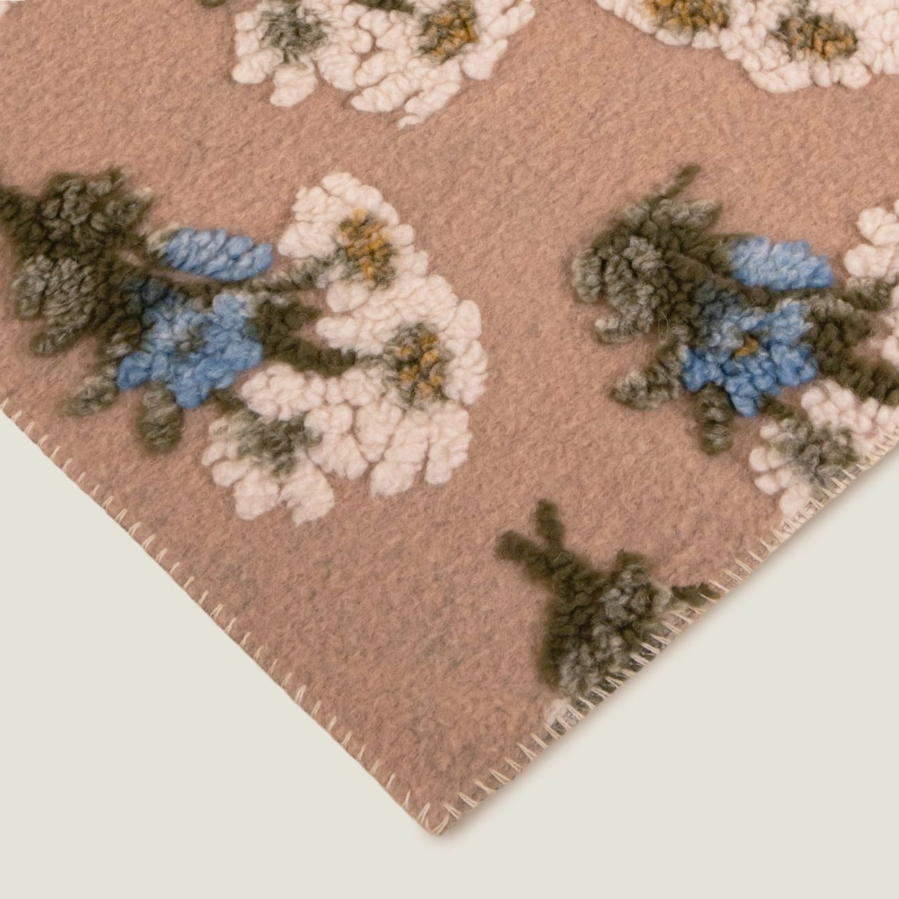Beige boiled wool throw with a white, blue and green floral pattern throughout.