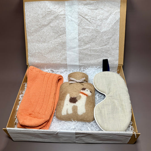 Gift box with orange ribbed alpaca socks, a natural linen coloured eye mask and a felted mini hot water bottle with a terrier dog design.