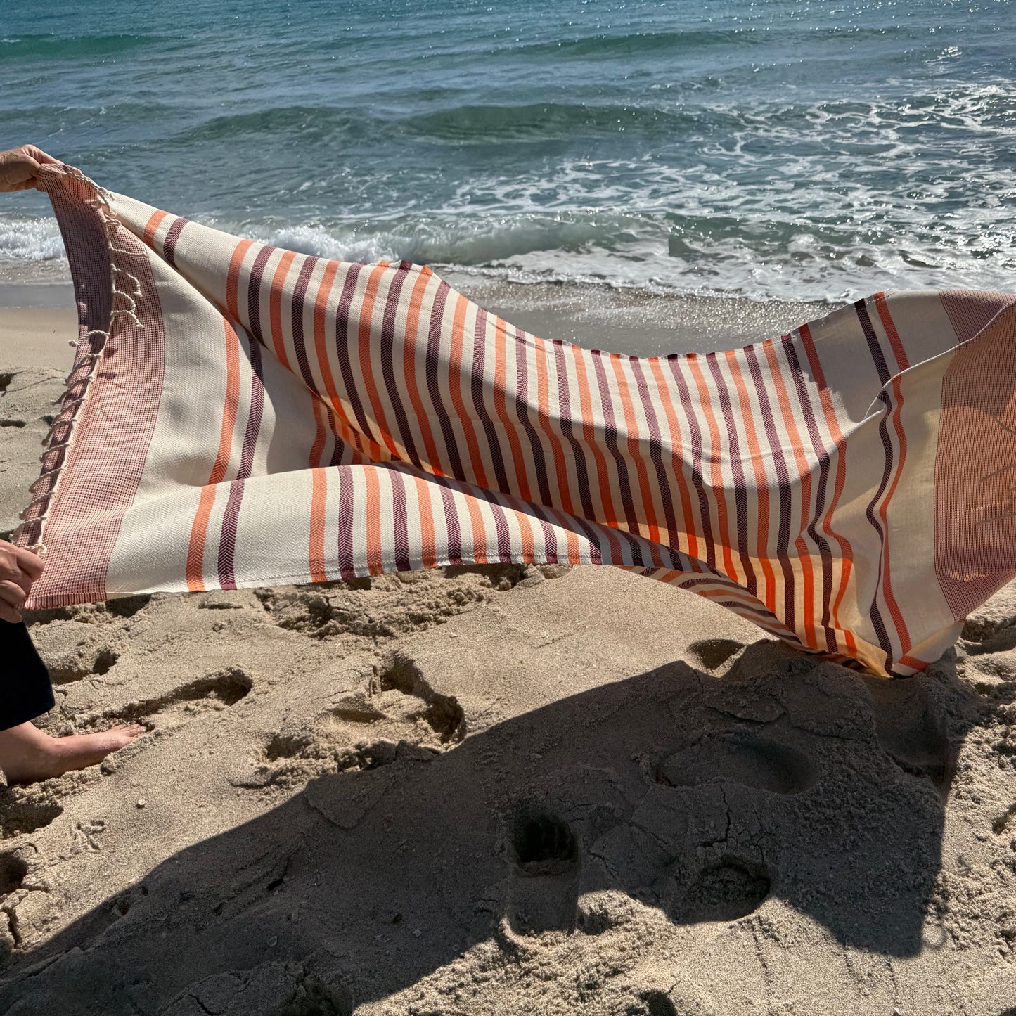 Antibes orange fouta beach towel shown blowing in the wind on the beach.