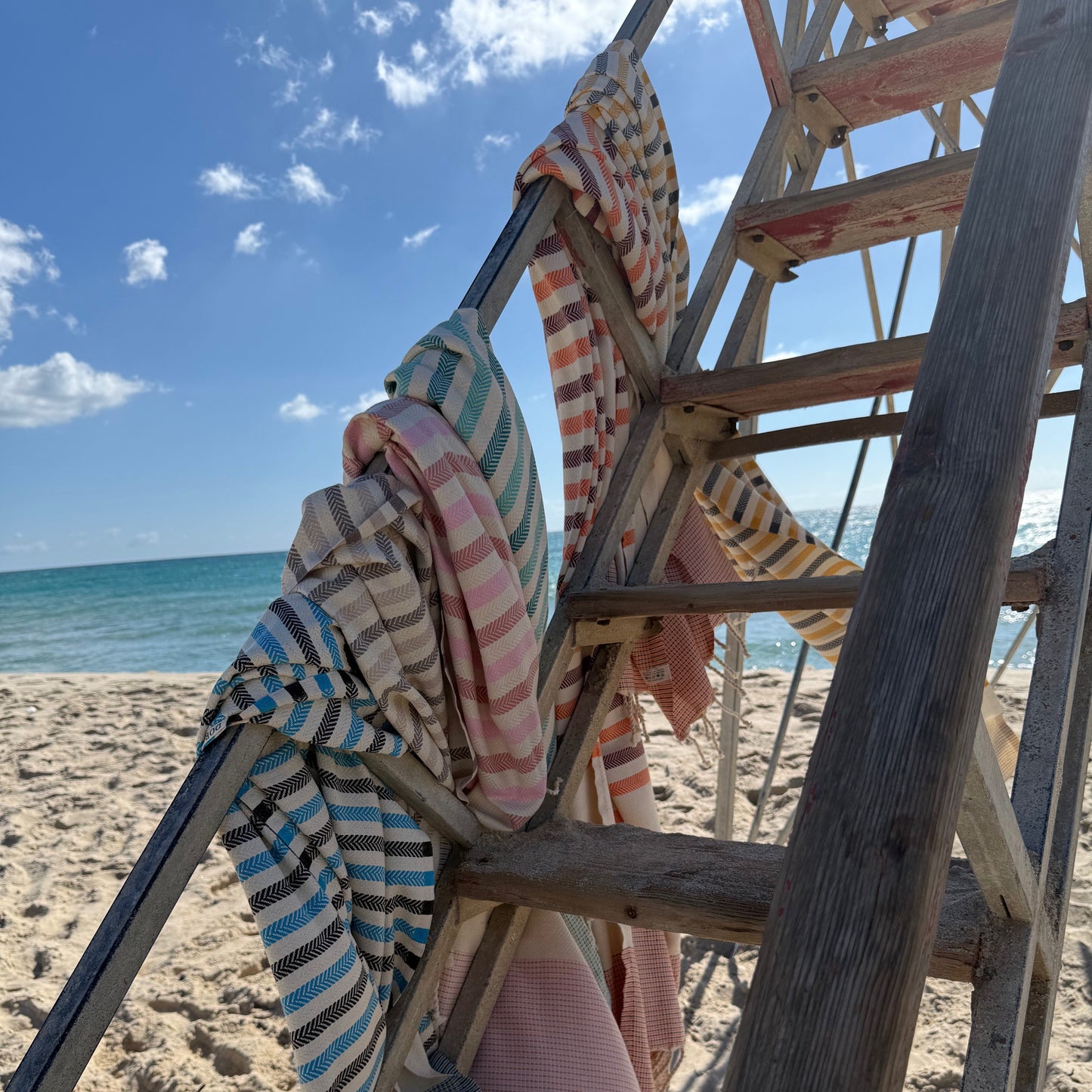 Colorful striped towels draped over a wooden lifeguard stand on a sandy beach with ocean view.