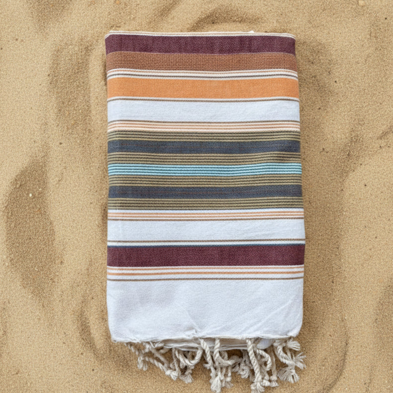 Burgundy, orange and white striped beach towel with a fringed edge.