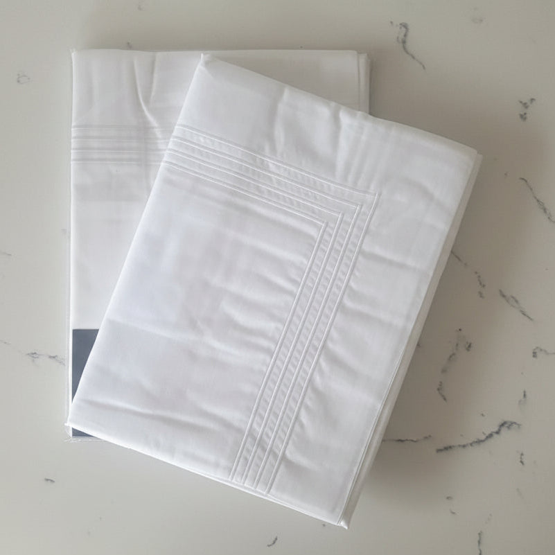 4 row white cord detailed king sized white pillowcases shown folded.