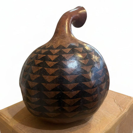 Decorative wooden gourd with geometric pattern on a wooden block in a room setting.