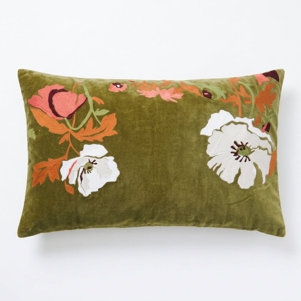 An olive green velvet rectangular lumbar pillow featuring embroidered floral motifs in pink, white, and orange, set against a clean light blue background.