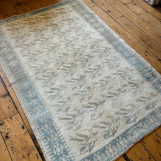 Handmade turkish rug with a light blue border and beige design in the middle.