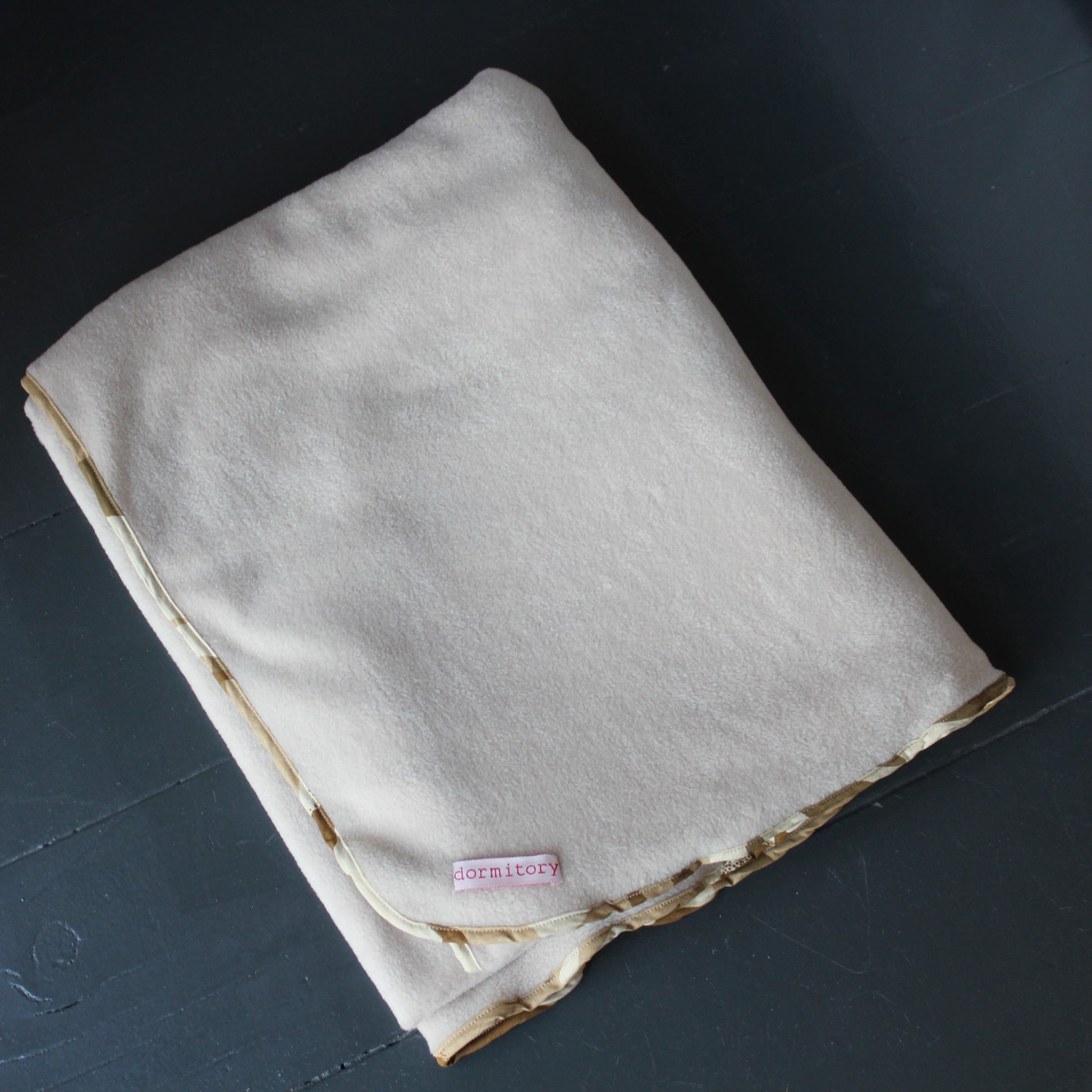 Folded beige blanket with a label on a dark surface