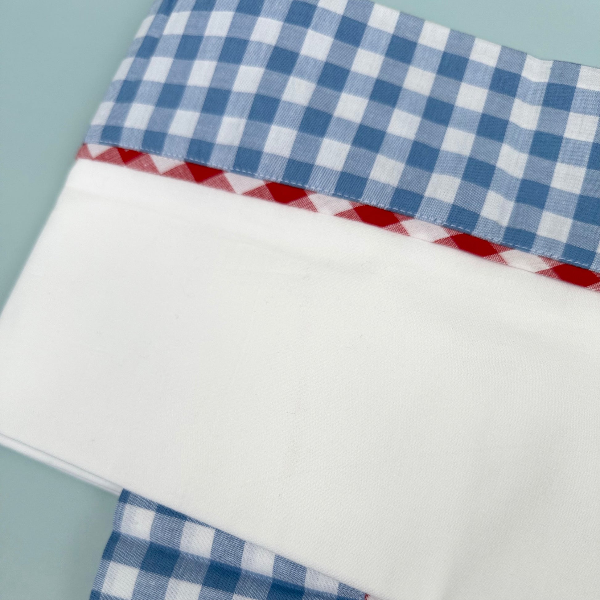 Detail of blue and red cotton gingham on the edge of a white cotton sheet