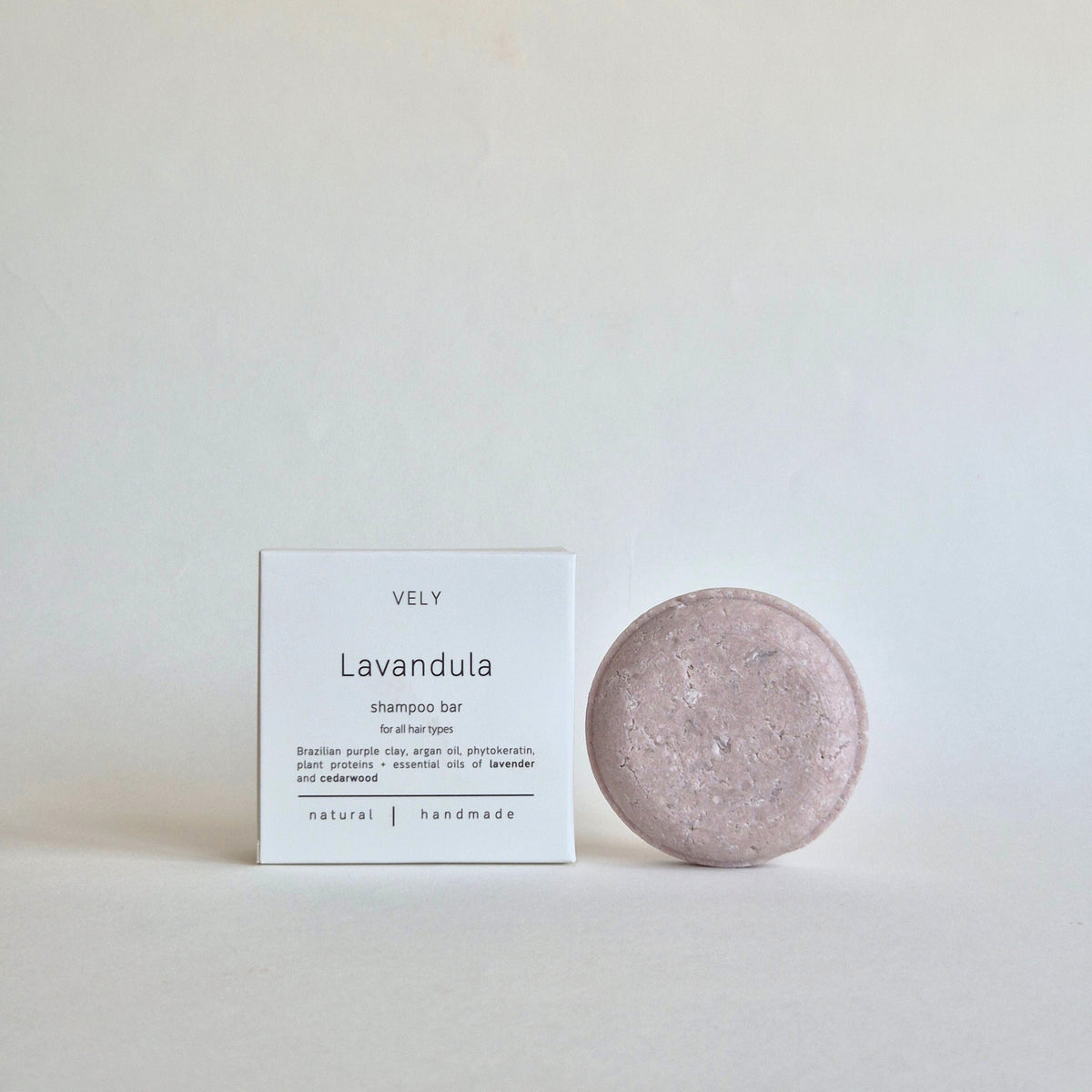A lavender shampoo bar next to its white packaging box, labeled 'VELY Lavandula shampoo bar', on a neutral light gray background.