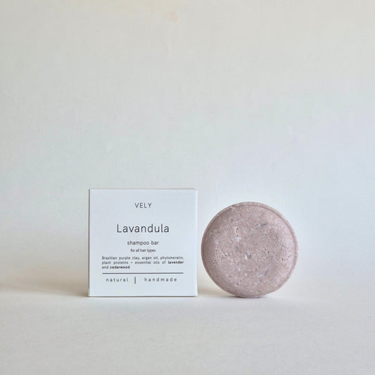 A lavender shampoo bar next to its white packaging box, labeled 'VELY Lavandula shampoo bar', on a neutral light gray background.