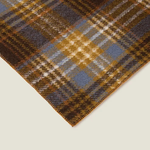 A close-up of a plaid fabric corner showing a woven pattern in brown, blue, gold, and white on a light beige background.
