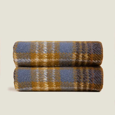 Two folded woven blankets stacked vertically, featuring a plaid pattern in slate blue, mustard yellow, and cream, set against a solid light beige background.