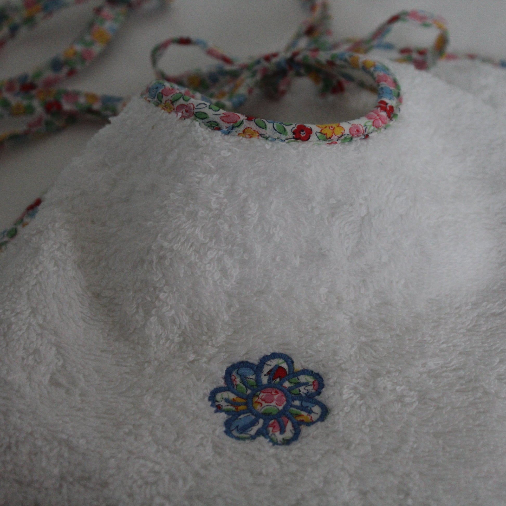 White bib with floral trim and embroidered flower design on a light background