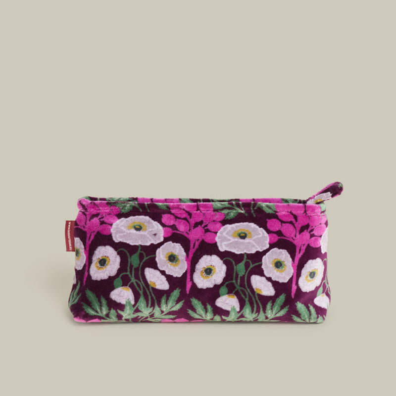 A small zippered pouch with a dark purple velvet-like fabric and an all-over floral print in pink, white, and green, shown against a solid light beige background.
