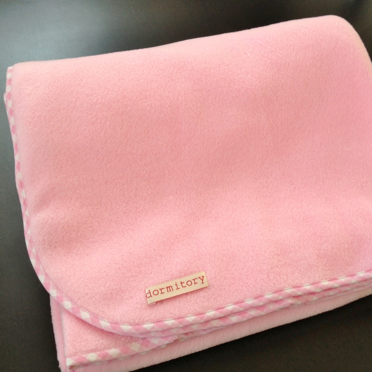 Pink blanket with 'dormitory' label on a dark surface