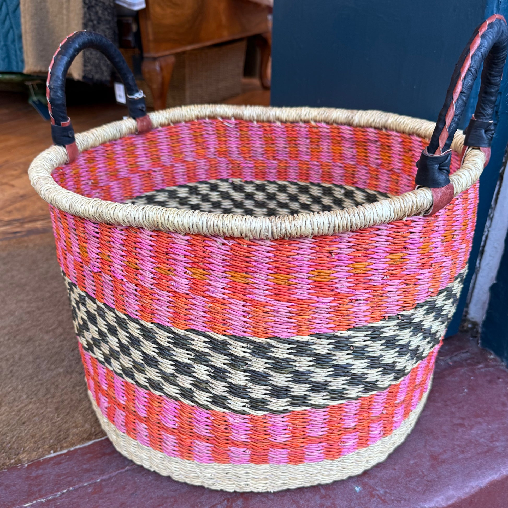 Hand woven large basket with pattern in pink, orange and black with leather covered handles