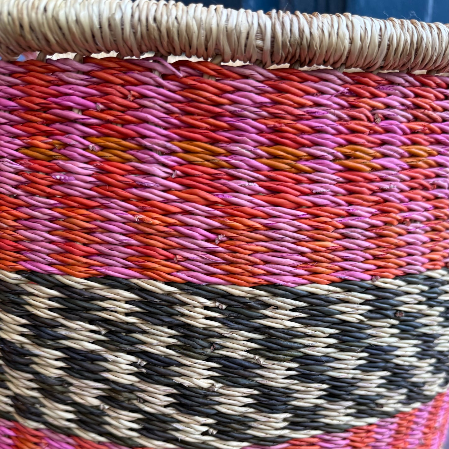 Close up detail of hand woven large basket with pattern in pink, orange and black.
