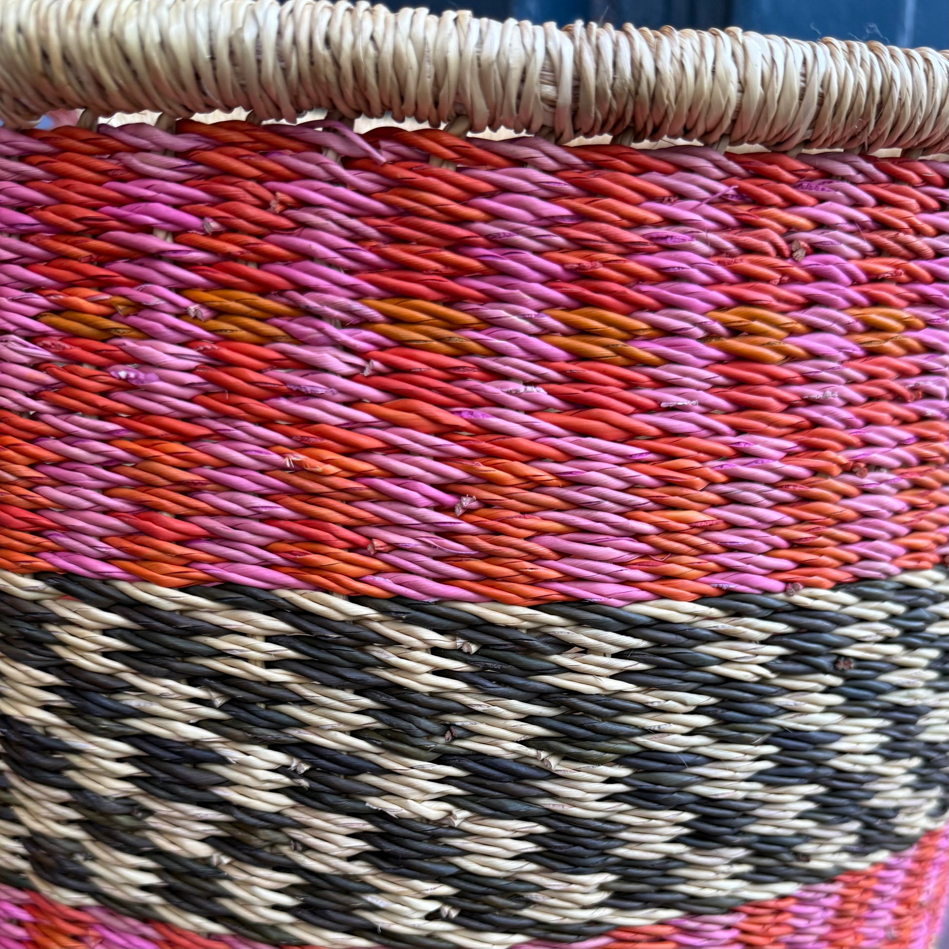 Close up detail of hand woven large basket with pattern in pink, orange and black.