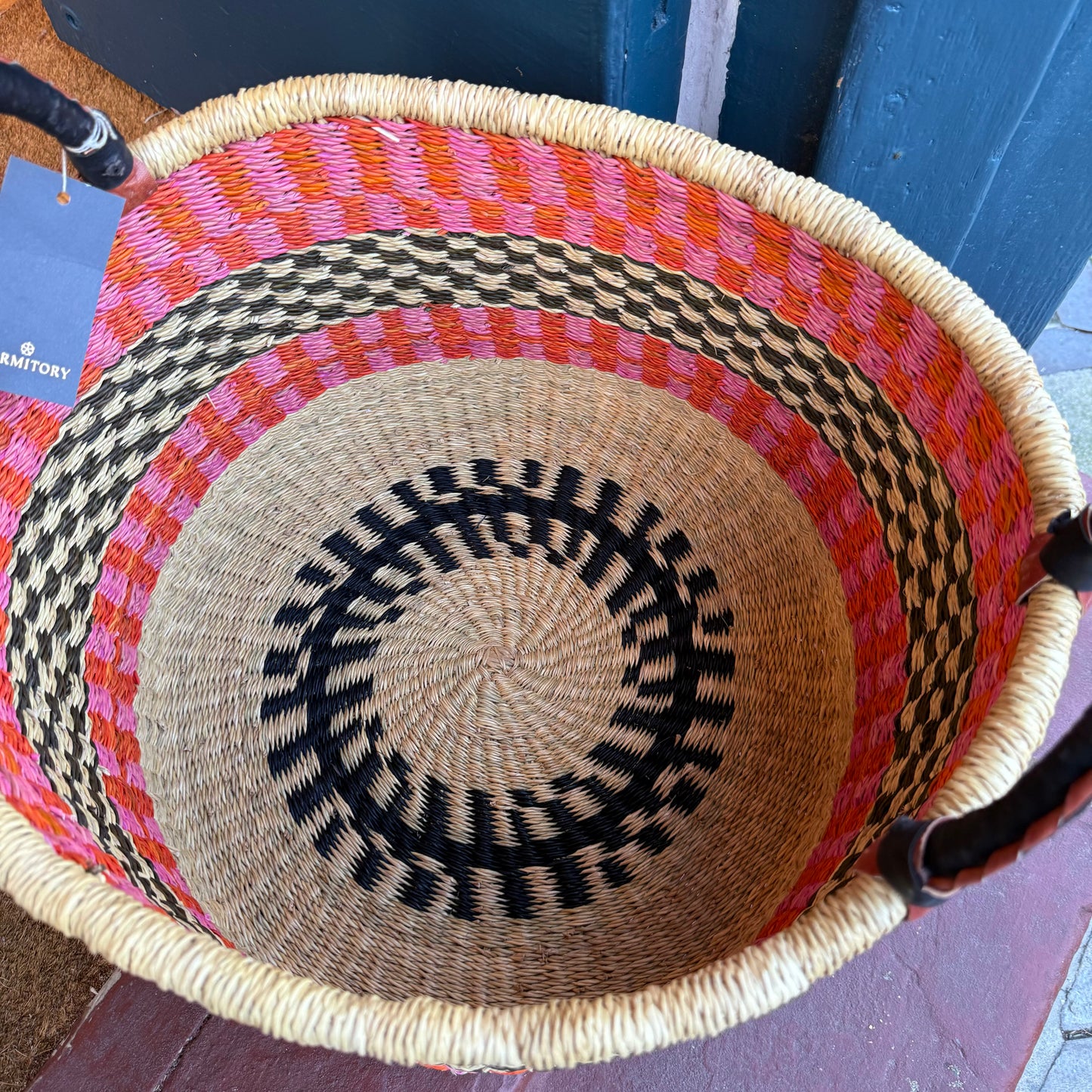 Inside of hand woven large basket with pattern in pink, orange and black with leather covered handles