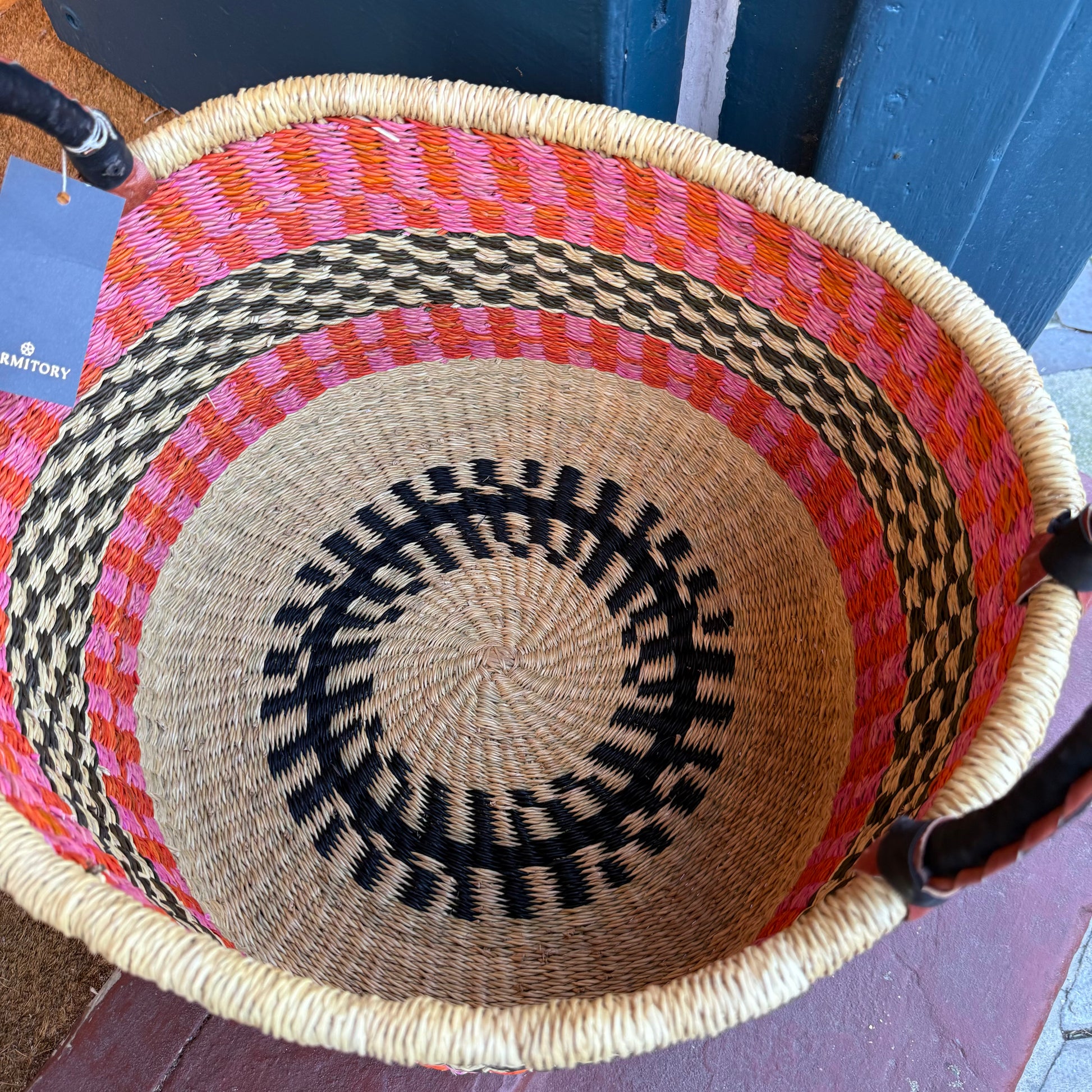 Inside of hand woven large basket with pattern in pink, orange and black with leather covered handles