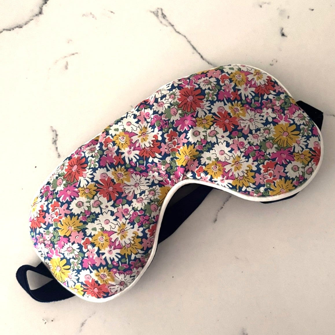 Multi coloured flower patterned eye mask with a white cording edge filled with lavender.