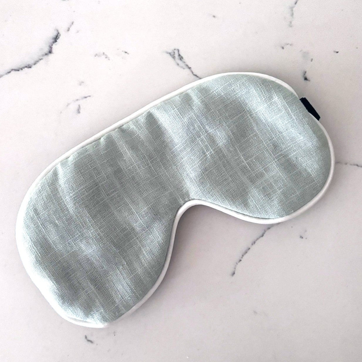Linen eye mask in baby blue with a white cording edge.